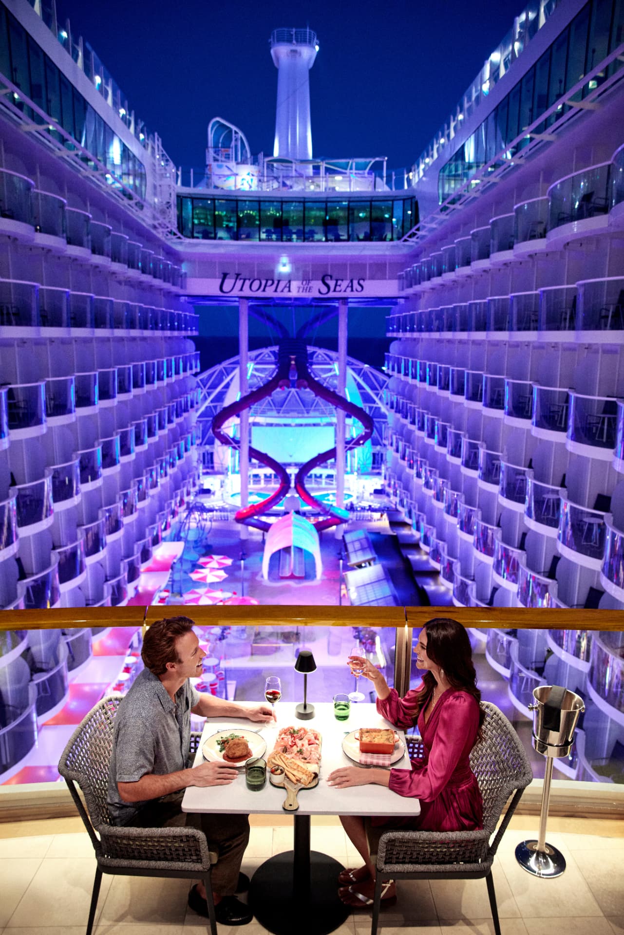 Guests seated together at a dining table overlooking the illuminated Boardwalk aboard Utopia of the Seas