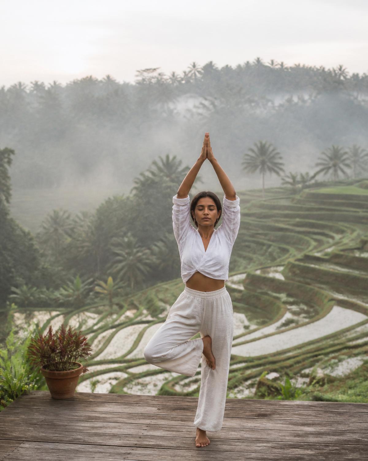 A woman practices morning yoga on a wooden platform above a rice terrace in Bali